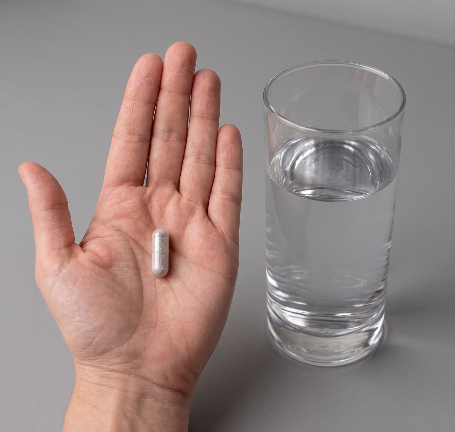 One capsule in hand beside a glass of water